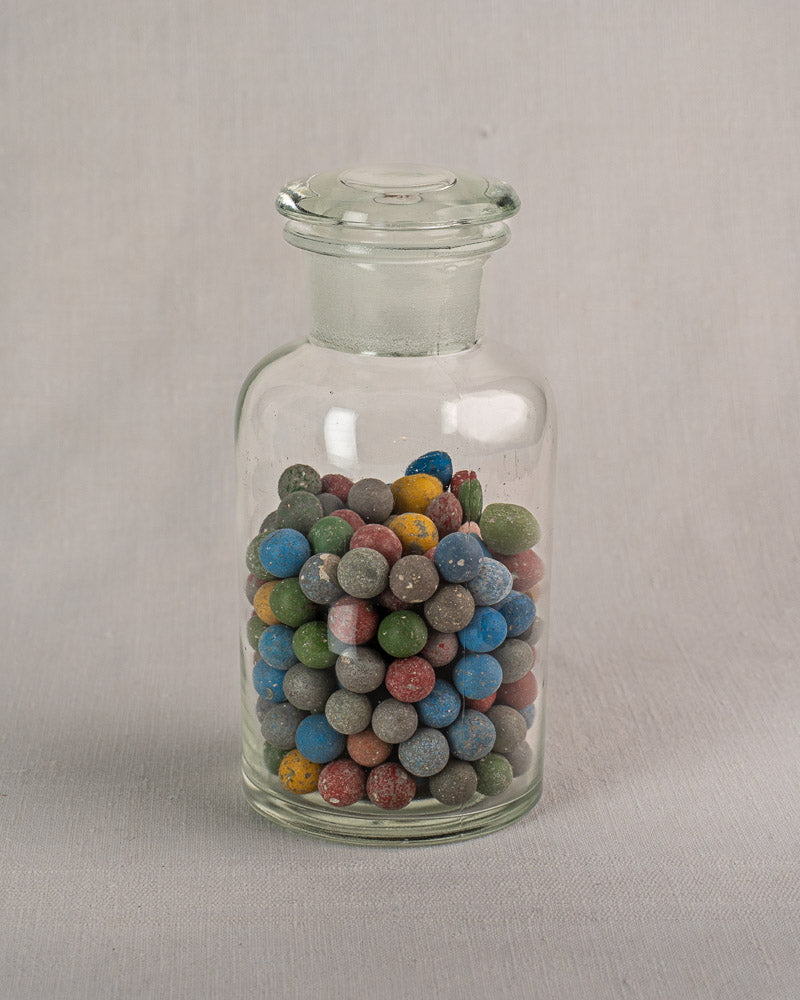 Antique French apothecary jar circa 1900 with multicolored clay marbles on a light gray surface.