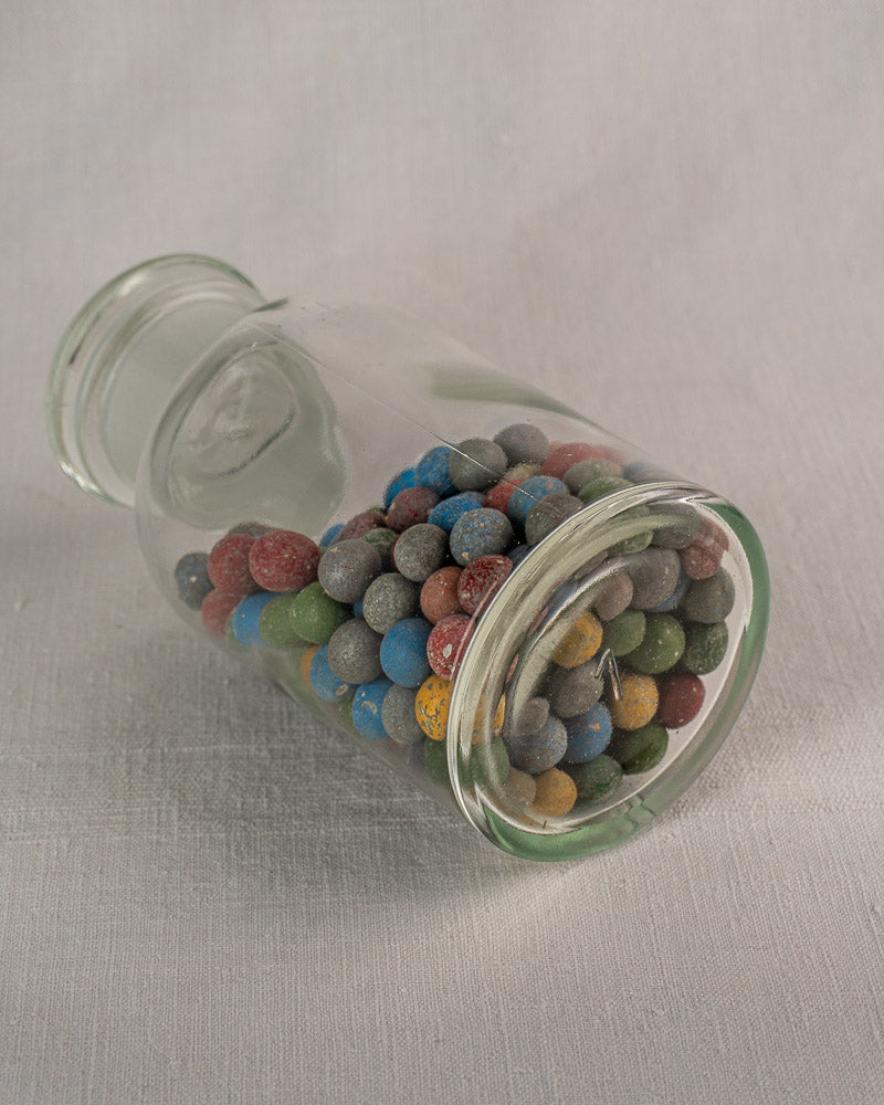Antique French apothecary jar from circa 1900, filled with colorful clay marbles on light fabric.