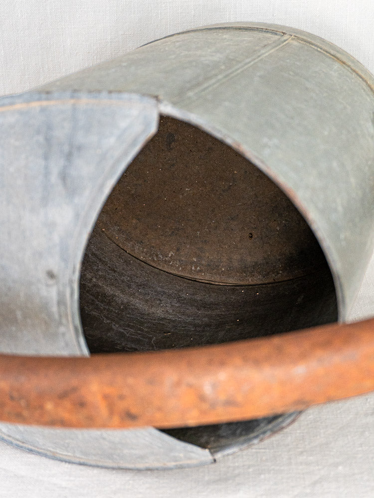 French zinc antique oval watering can with weathered patina, rusted handle, and visible open interior.