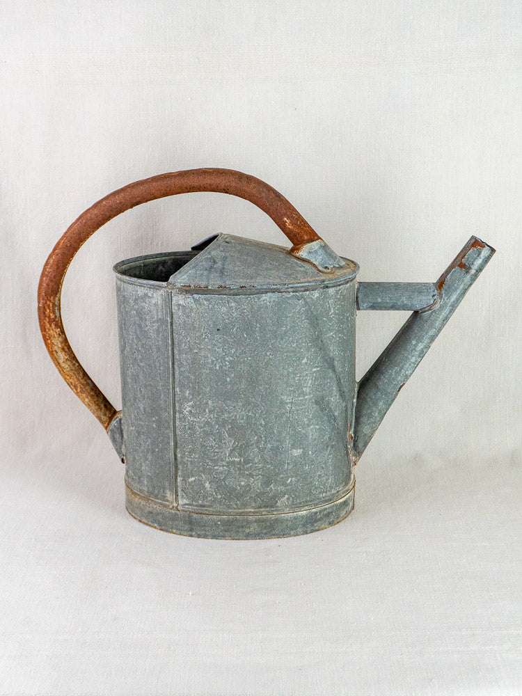 Antique French zinc oval watering can with large handle and straight spout on plain surface.