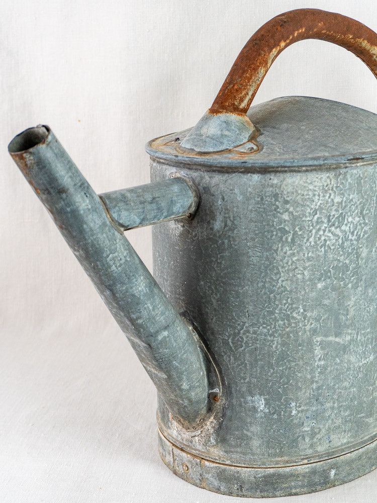 French antique oval zinc watering can with a weathered body, rusty handle, and straight spout.