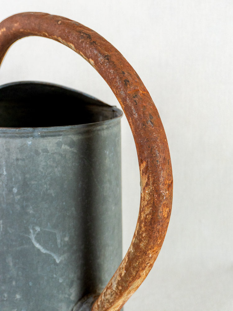 French antique oval zinc watering can with weathered metal and rusted handle on light background.