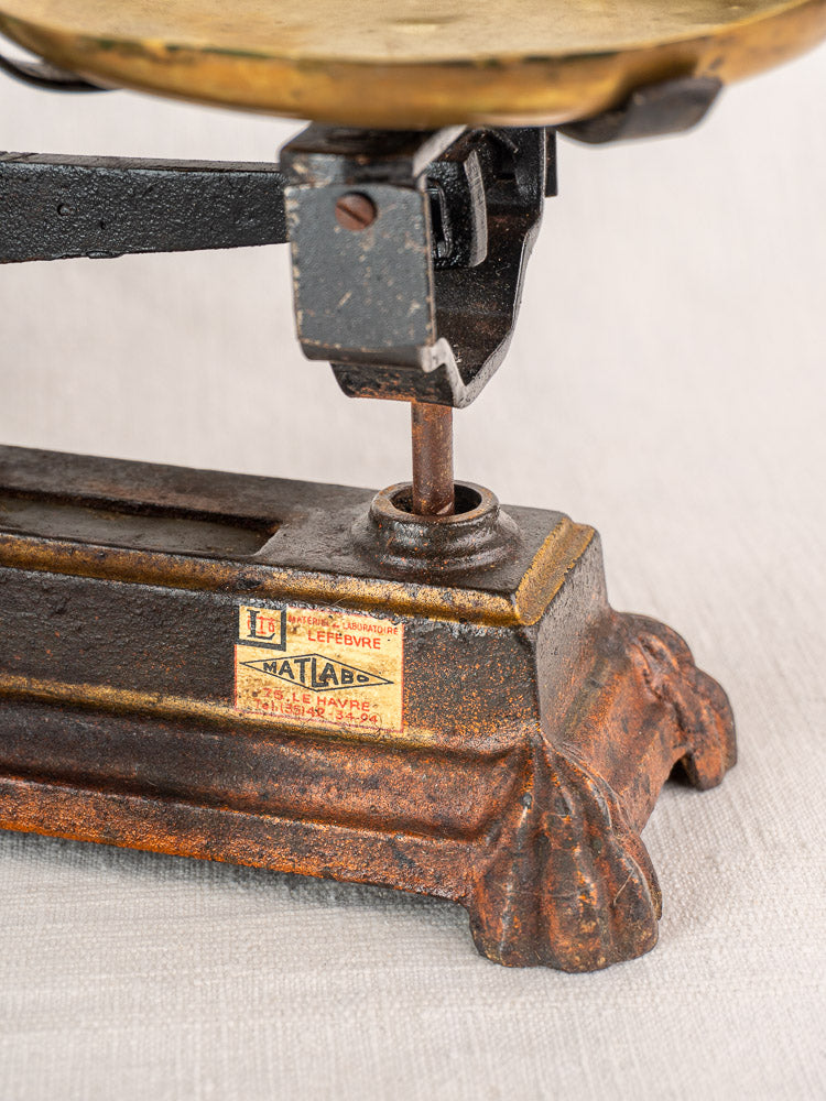 Antique French Roberval cast iron and brass balance scale base with yellowed label and rust on a light textured surface.
