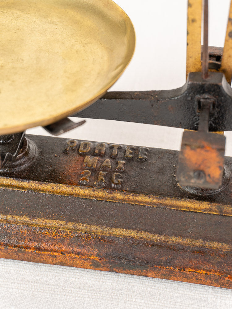 Antique French Roberval balance scale with brass pan and cast iron base marked “PORTEE MAX 2 KG”.