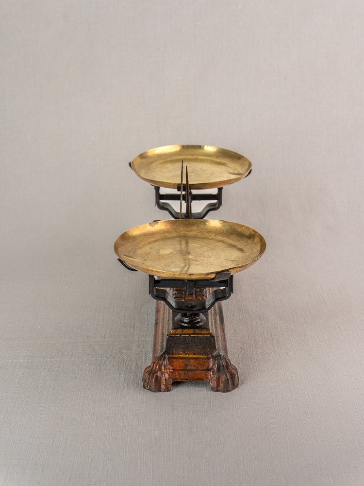 Antique French Roberval balance scale in cast iron and brass with dual trays on a wooden base, plain light gray backdrop.