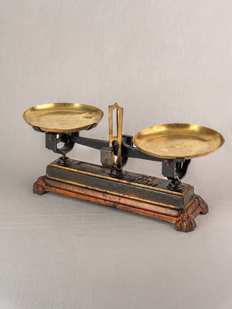 Antique French cast iron and brass Roberval balance scale with twin round brass pans on a neutral background.