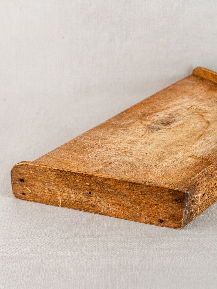 Antique French beech cutting board, late 19th century, with raised edge on neutral fabric.