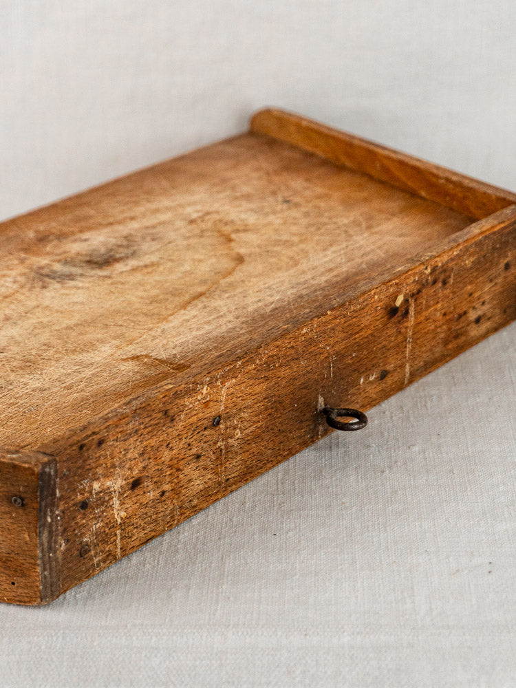 Late 19th-century French beech cutting board with raised edges, metal ring, on light fabric.