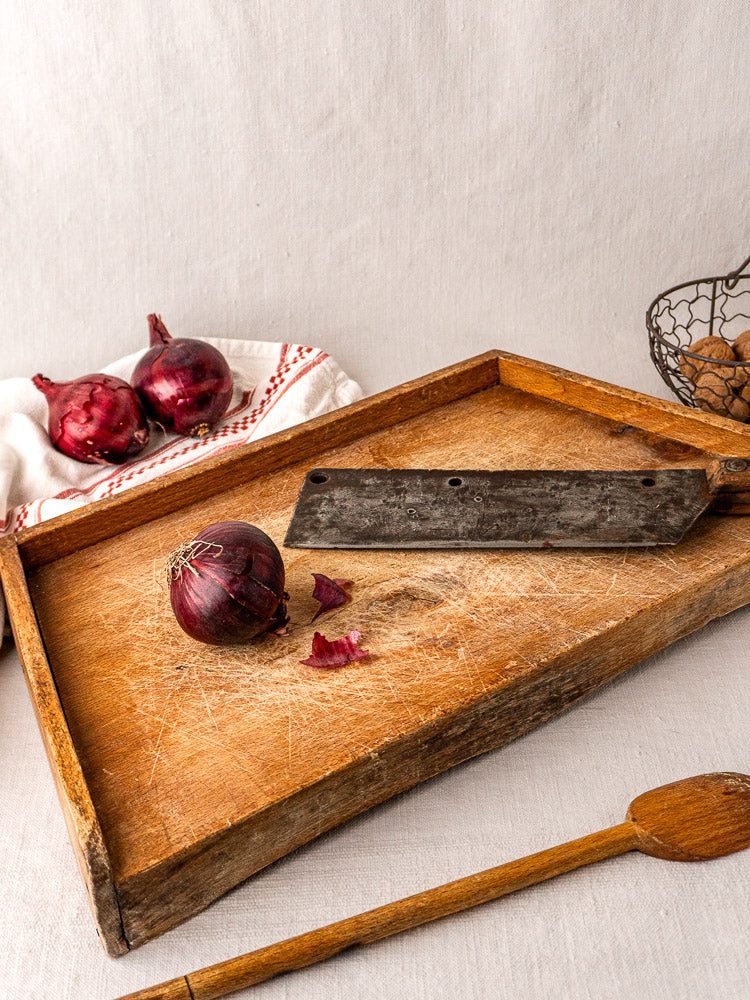 Antique French beech cutting board with red onion, old knife, and wooden tray; potatoes and spoon nearby.
