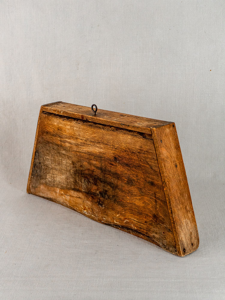 Late 19th-century French beech cutting board with trapezoidal form and metal hook on light gray surface.