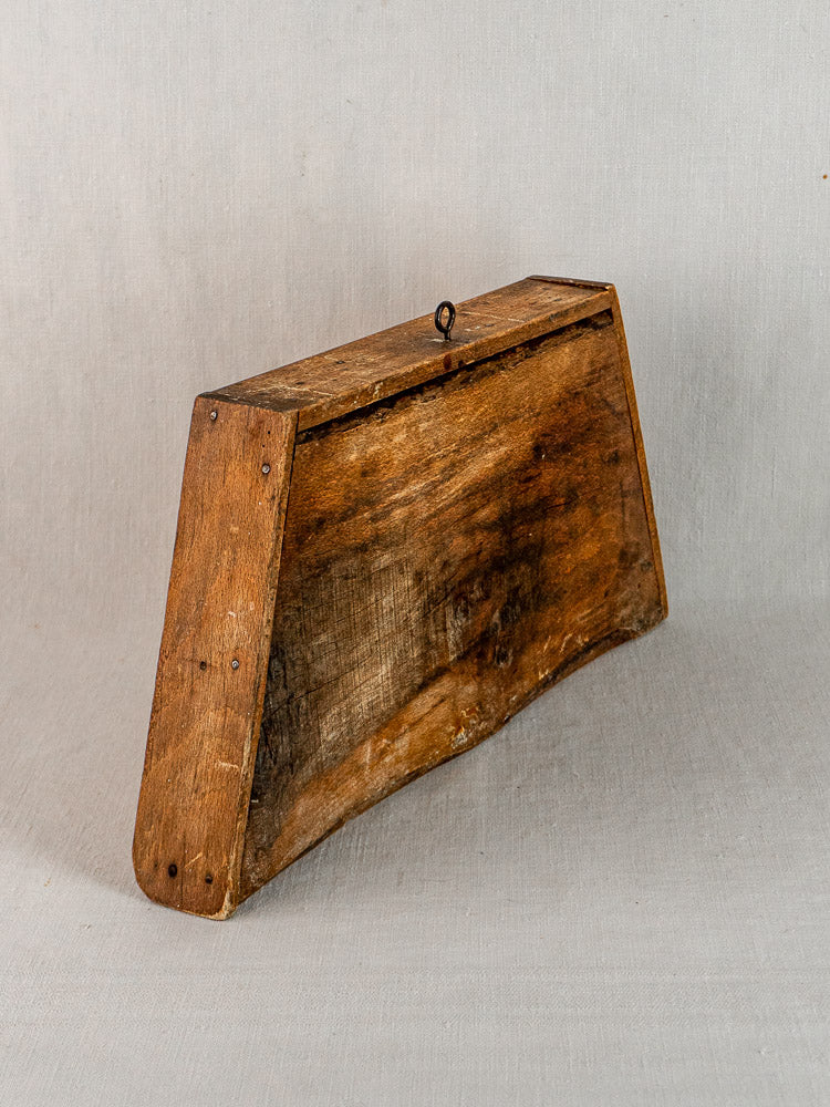 Late 19th-century French beech cutting board with trapezoid shape, nail details, and metal loop, on light gray background.