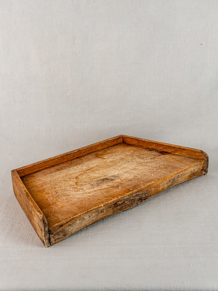 Antique French beechwood cutting board with raised edges and worn texture on gray fabric.