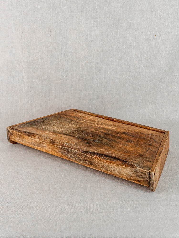 Late 19th-century antique French beech cutting board with raised edges on neutral fabric background.