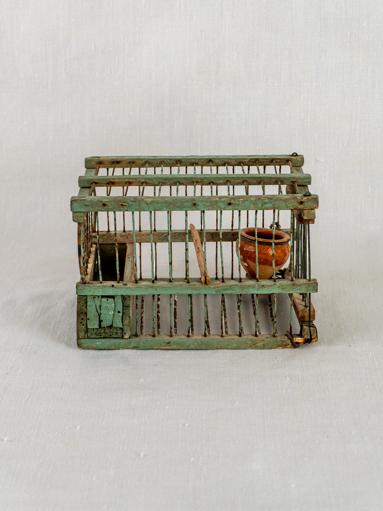 Petite antique French sage green metal decoy bird cage with rustic finish, perch, and clay water pot.