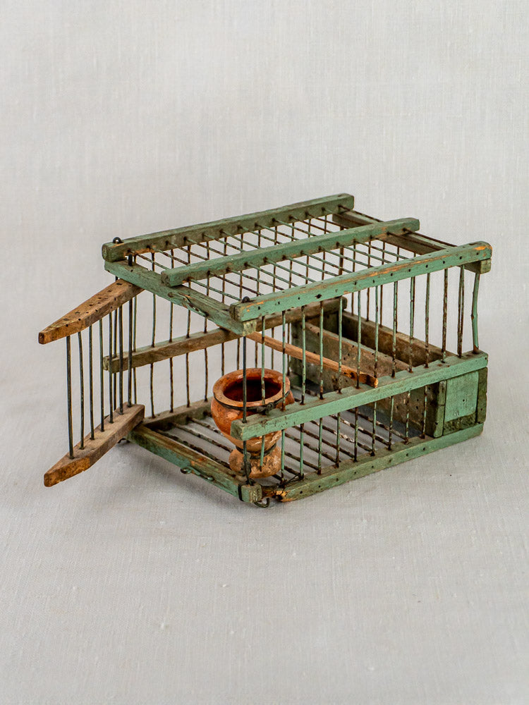 Antique sage green French birdcage with open door, featuring a small clay pot inside.