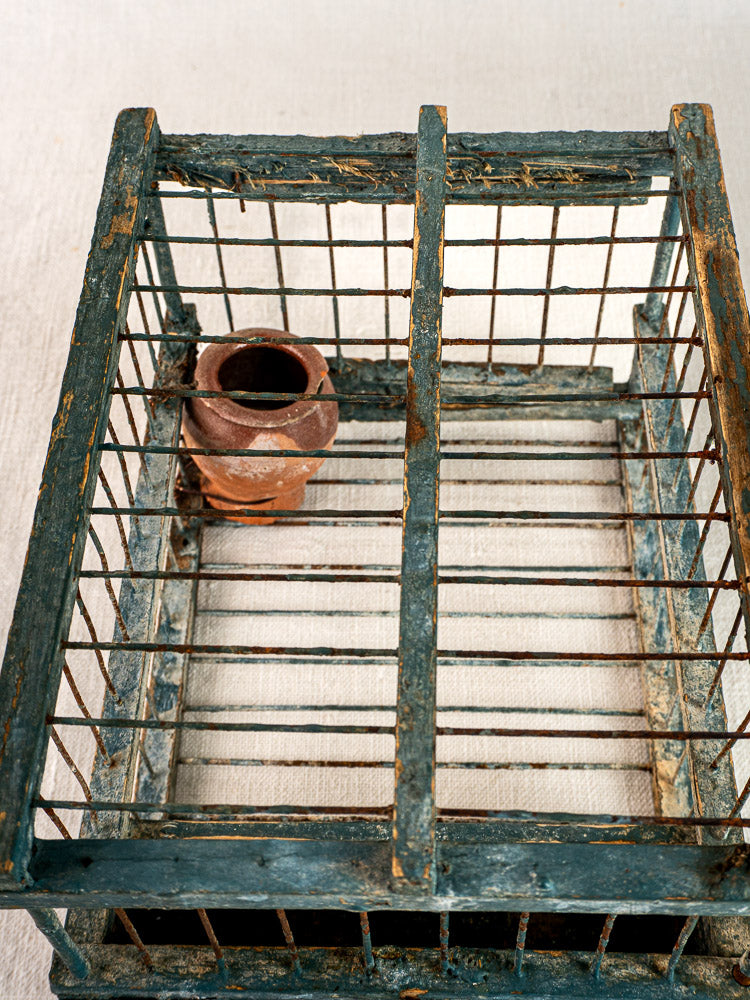 Provençal bird cage with terracotta cup and original blue paint, late 19th century, on light fabric. Weathered vintage patina.