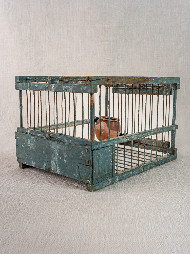 Late 19th-century Provençal bird cage with original blue paint and terracotta cup, displayed on a woven surface.