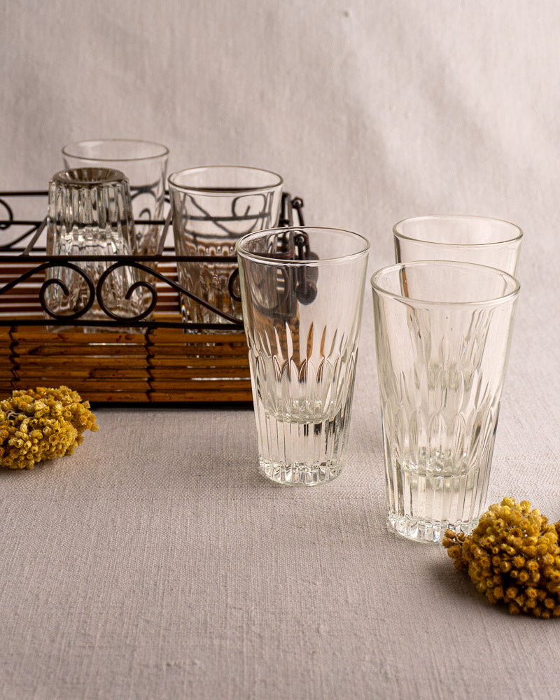 Set of six fluted tumblers in a wrought iron and rattan French bistro caddy with yellow florals on light linen.