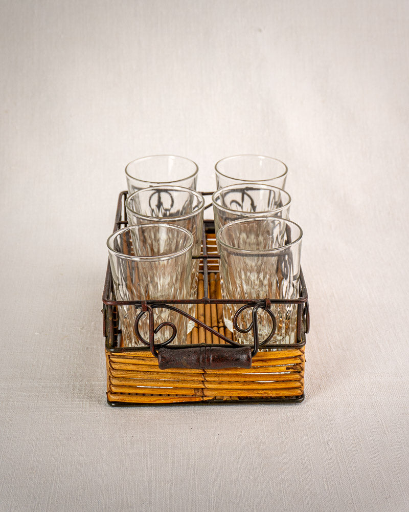 Vintage French bistro glass caddy in wrought iron and rattan with six fluted tumblers, on a light background.