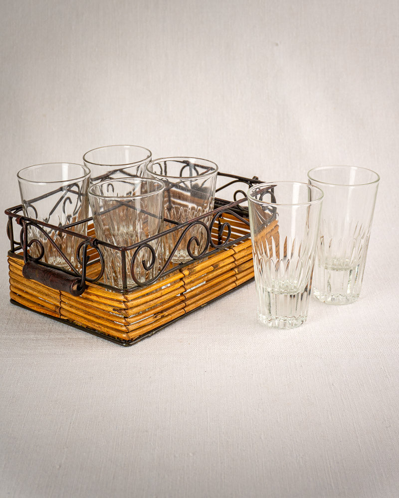 Set of six fluted French bistro tumblers, four in wrought iron and rattan caddy, two beside on light surface.