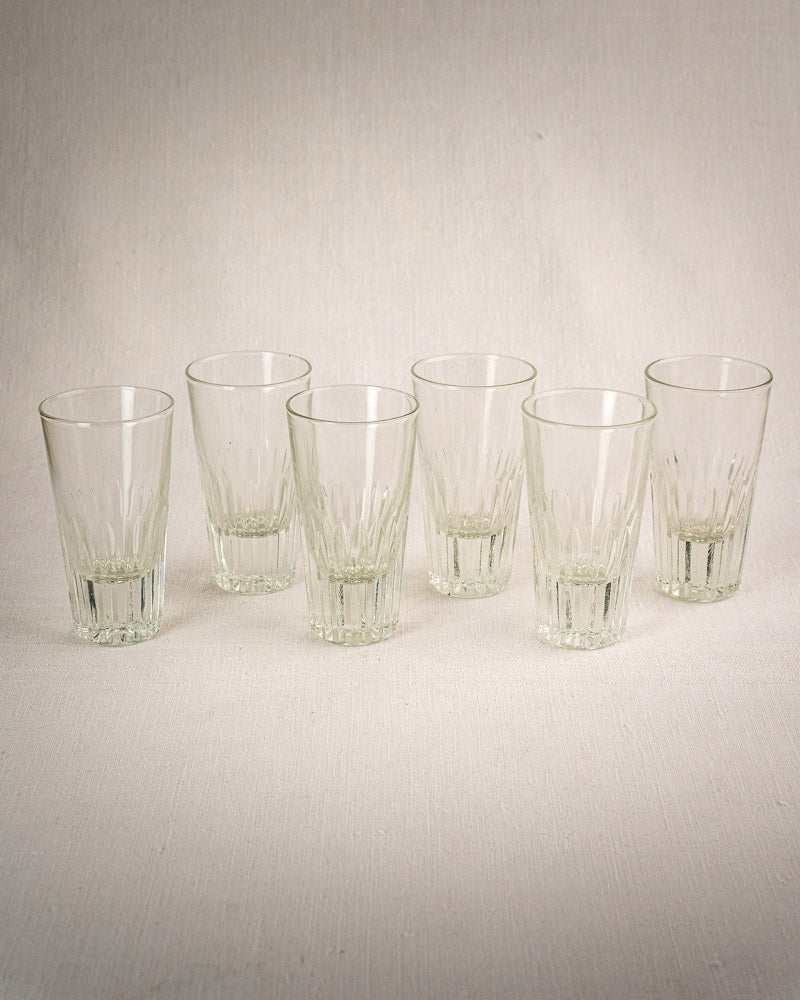 Set of six fluted French bistro tumblers in wrought iron and rattan caddy on light textured surface.
