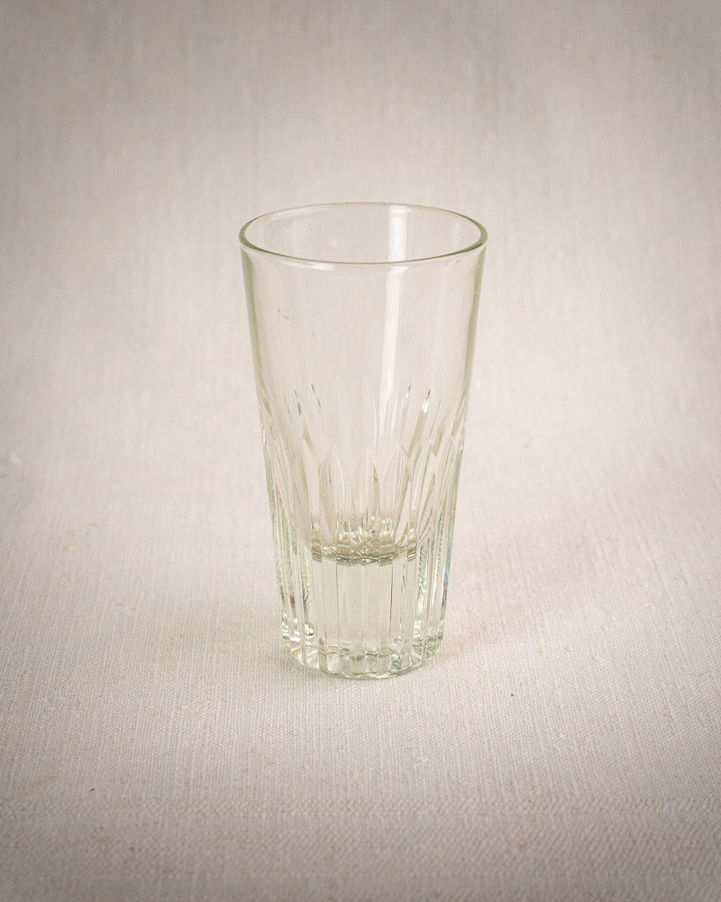 Set of six fluted tumblers on light textured surface, in vintage French bistro wrought iron and rattan glass caddy.
