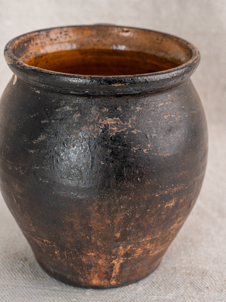 Antique French Provincial glazed earthenware jug with wide opening, rounded base, and weathered brown-orange glaze on light fabric.