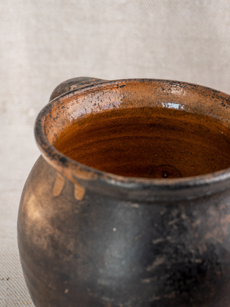 Antique French Provincial glazed earthenware jug with rustic dark brown finish, textured surface, and twin handles against neutral background.