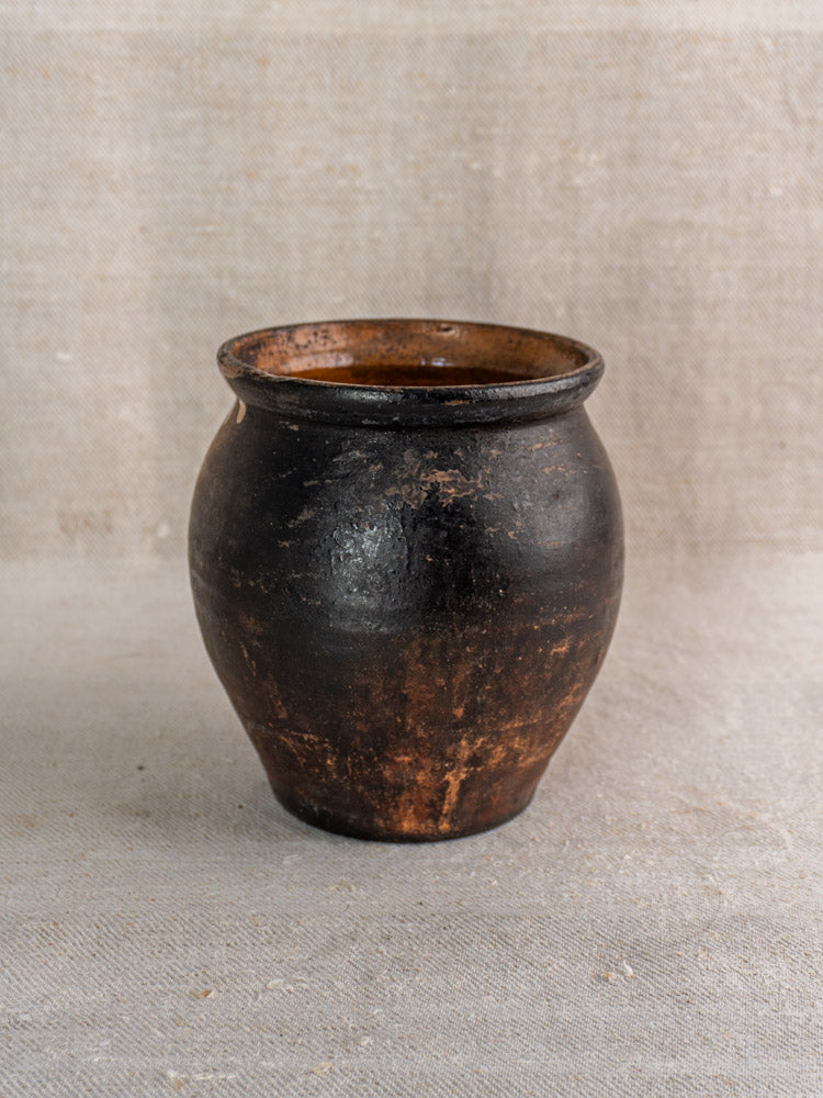 Antique French Provincial glazed earthenware jug with dark brown glaze, rounded body, and narrow opening on beige fabric.