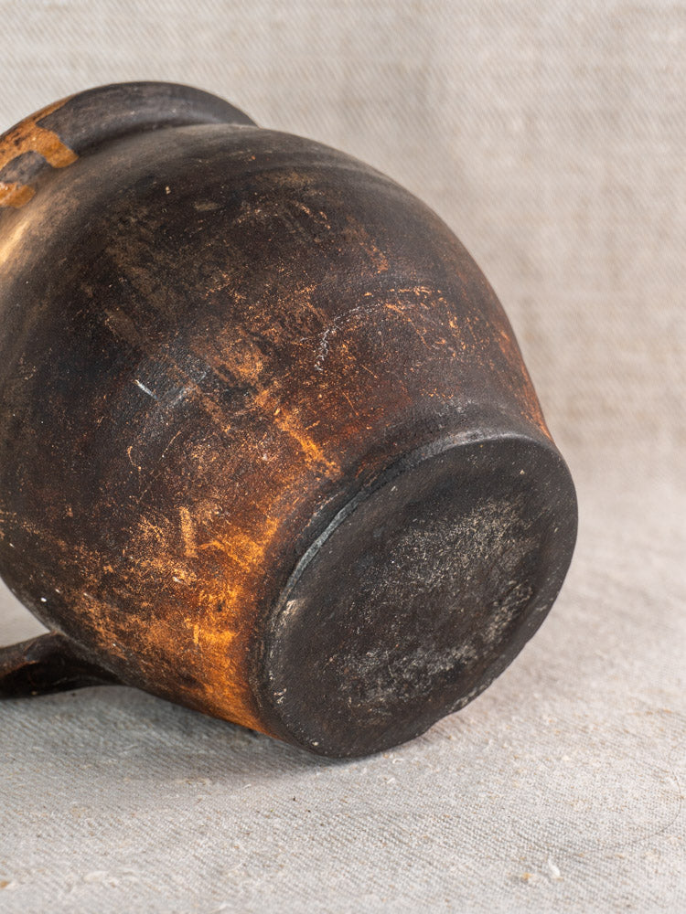 Bottom of antique French Provincial glazed earthenware jug displayed on textured fabric, showcasing rustic craftsmanship.