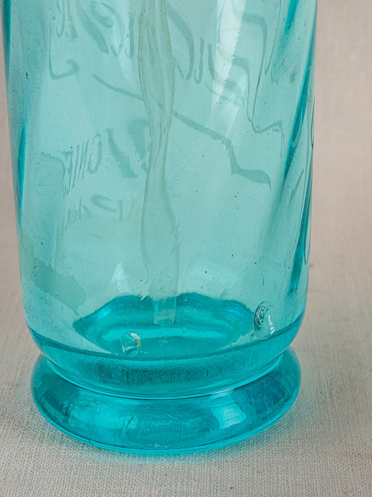 J. Dubuche antique French bistro seltzer bottle in blue glass with textured reflections, on light fabric.
