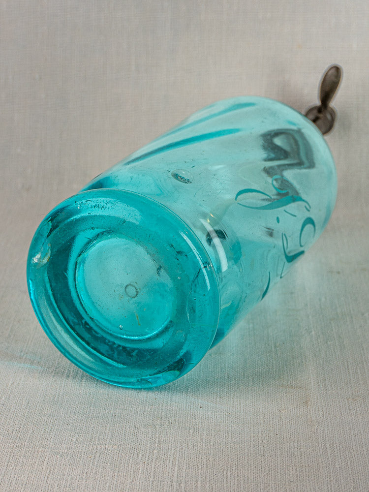 Turquoise glass tumbler with silver spoon inside, resting on light fabric, inspired by vintage French soda siphon.