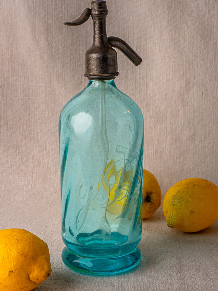 J. Dubuche antique French blue soda siphon with metal spout and three lemons on fabric.