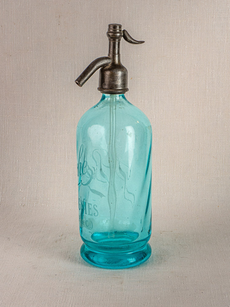 Antique French bistro seltzer bottle with blue glass and metal siphon top on light surface.
