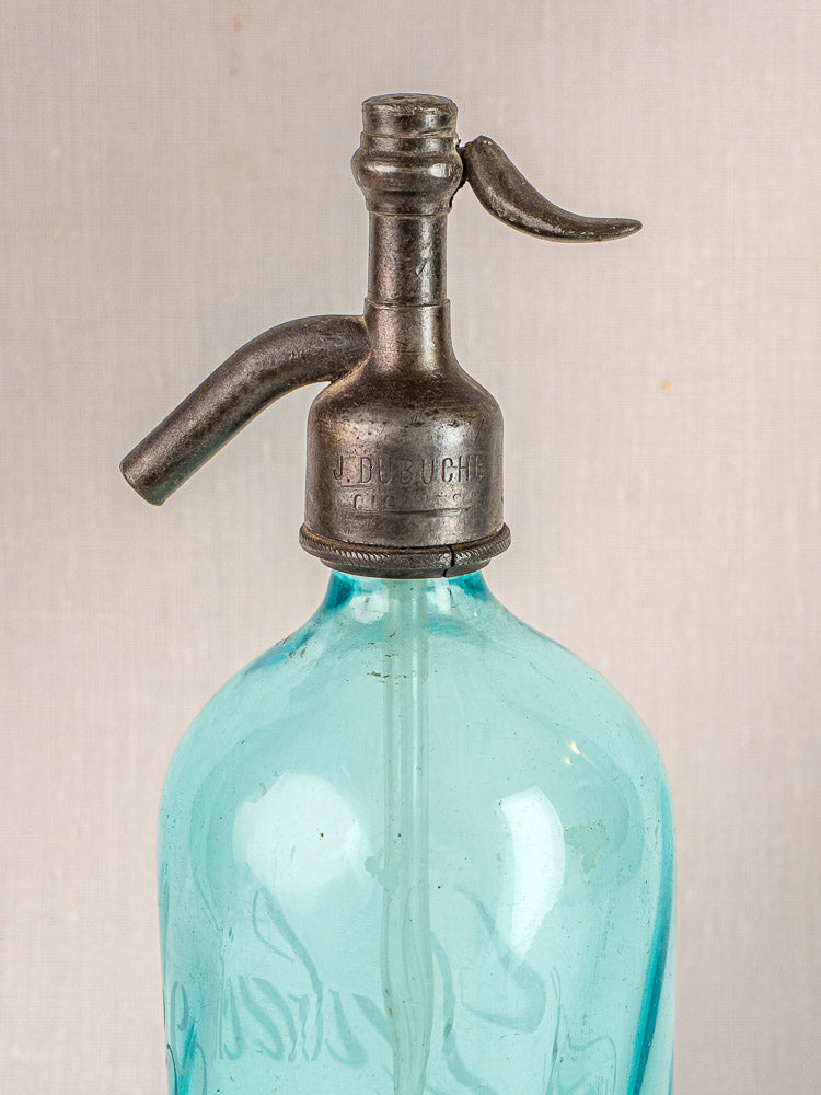J. Dubuche antique French soda siphon with blue glass and metal top on beige background.