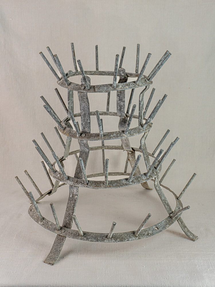 Antique French zinc bottle dryer, c. 1900, three tiers with pegs, displayed on light fabric against a neutral background.