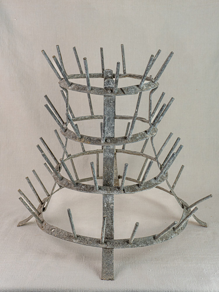 Antique French bottle dryer, circa 1900, galvanized zinc with four tiers and multiple pegs on neutral fabric background.