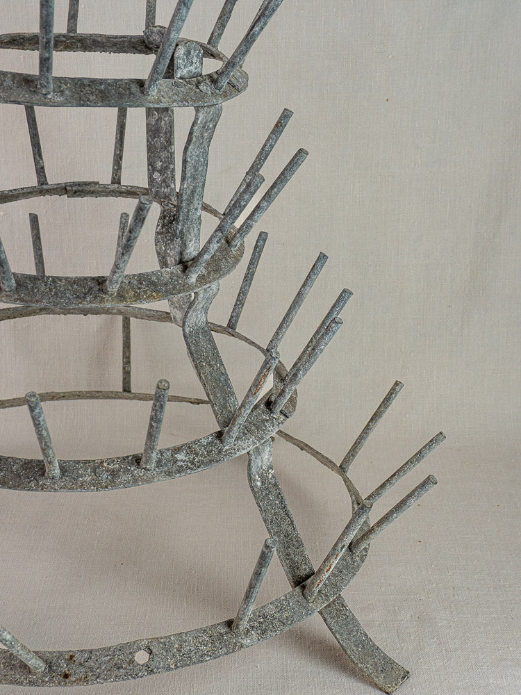 Antique French galvanized zinc bottle dryer, circa 1900, with four tiers and pegs on a neutral fabric background.