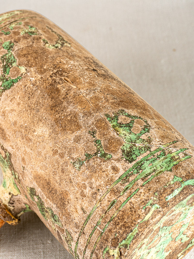 18th-century French terracotta Bouillotte with peeling green paint and textured brown surface on light gray fabric.
