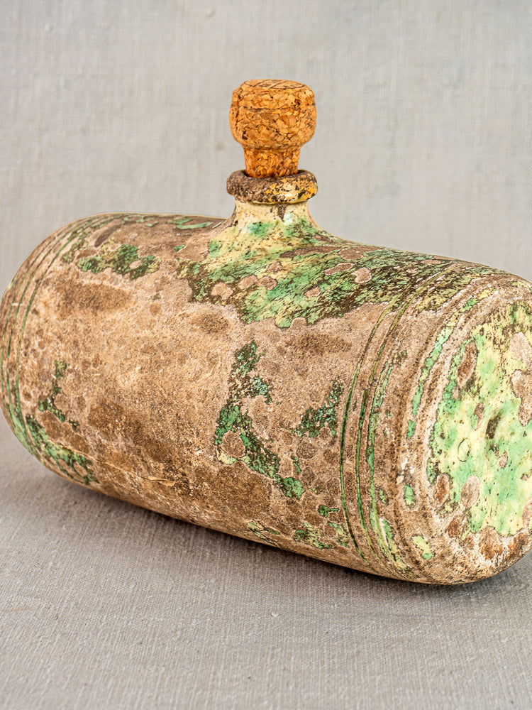 18th-century French terracotta bouillotte bed warmer with cork stopper and green-brown patina on neutral fabric background.