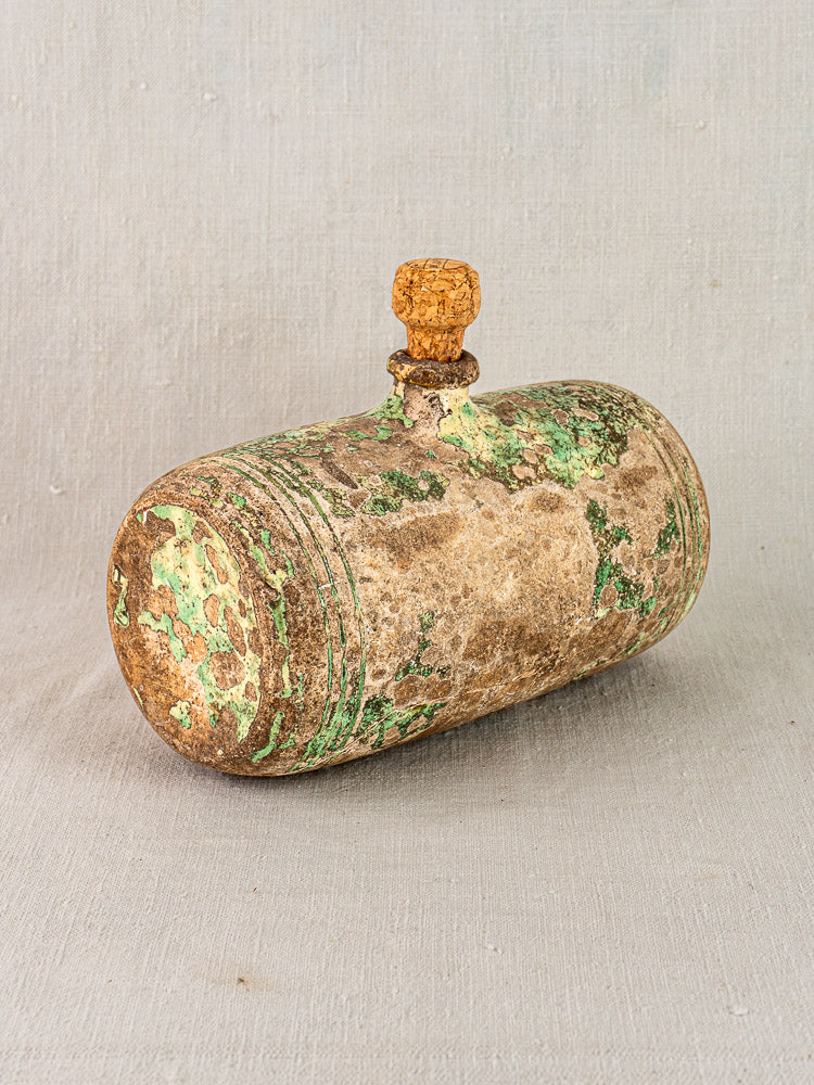 Antique 18th-century French terracotta Bouillotte with cork stopper and green patina, shown on neutral textured fabric.