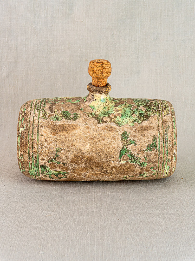 18th-century French terracotta Bouillotte hot water bottle with green patina and cork stopper on neutral fabric.