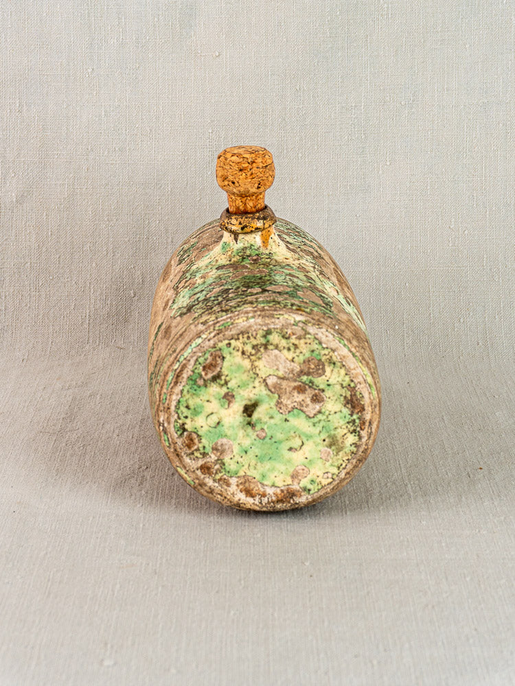 18th-century French terracotta Bouillotte with cork, weathered green and brown glaze, on neutral fabric backdrop.