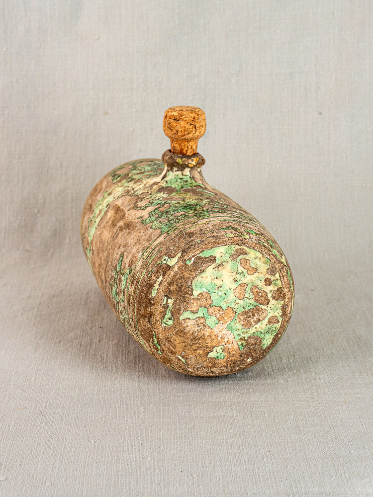 Antique French terracotta Bouillotte with cork stopper and green-brown patina on neutral fabric background.