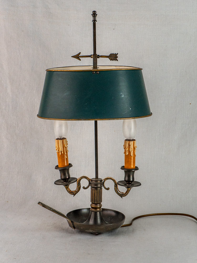 French Bouillotte lamp with vintage green tôle shade, brass base, and arrow finial on light background.