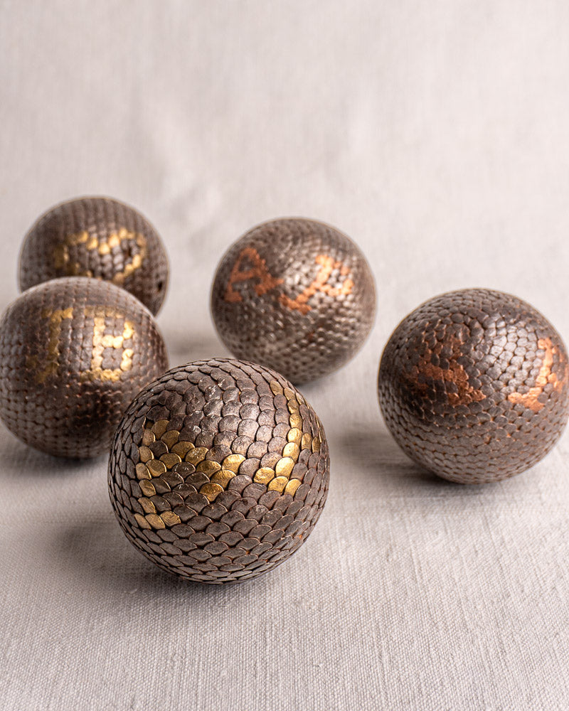 Set of five antique French Boules Cloutées with textured metal, gold or copper numbers on light fabric background.