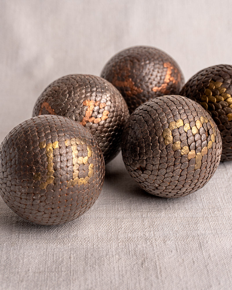 Set of five antique French Petanque balls with textured metallic surfaces and gold, copper accents on light gray fabric.