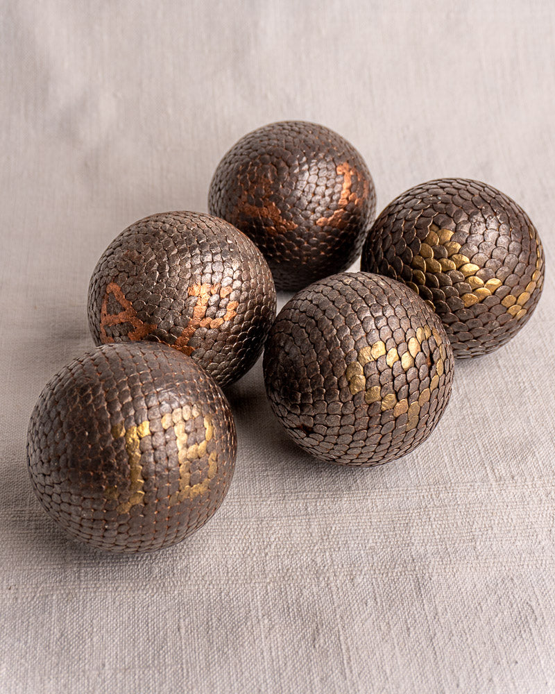 Five antique French boules cloutées, each with distinct gold or copper-toned symbols, on a light fabric surface.