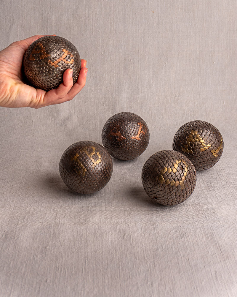 Antique French Boules Cloutées petanque ball held in hand, four matching boules on light gray surface behind.