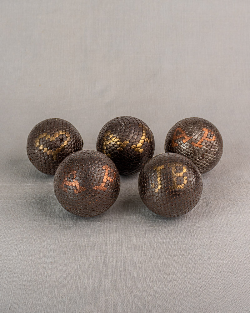 Five antique French petanque balls with textured, numbered surfaces on a plain gray fabric background. Early 20th century.